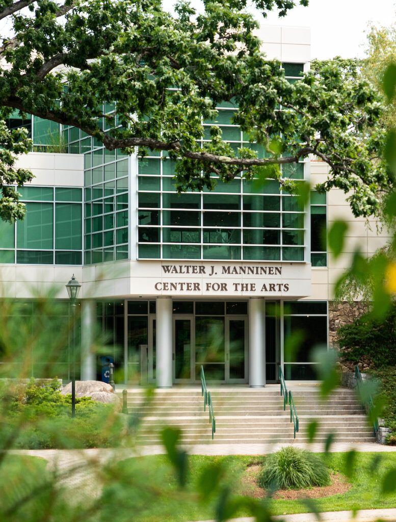 The Walter J. Manninen Center for the Arts at Endicott College — glass and pale stone framed by a broad oak branch.