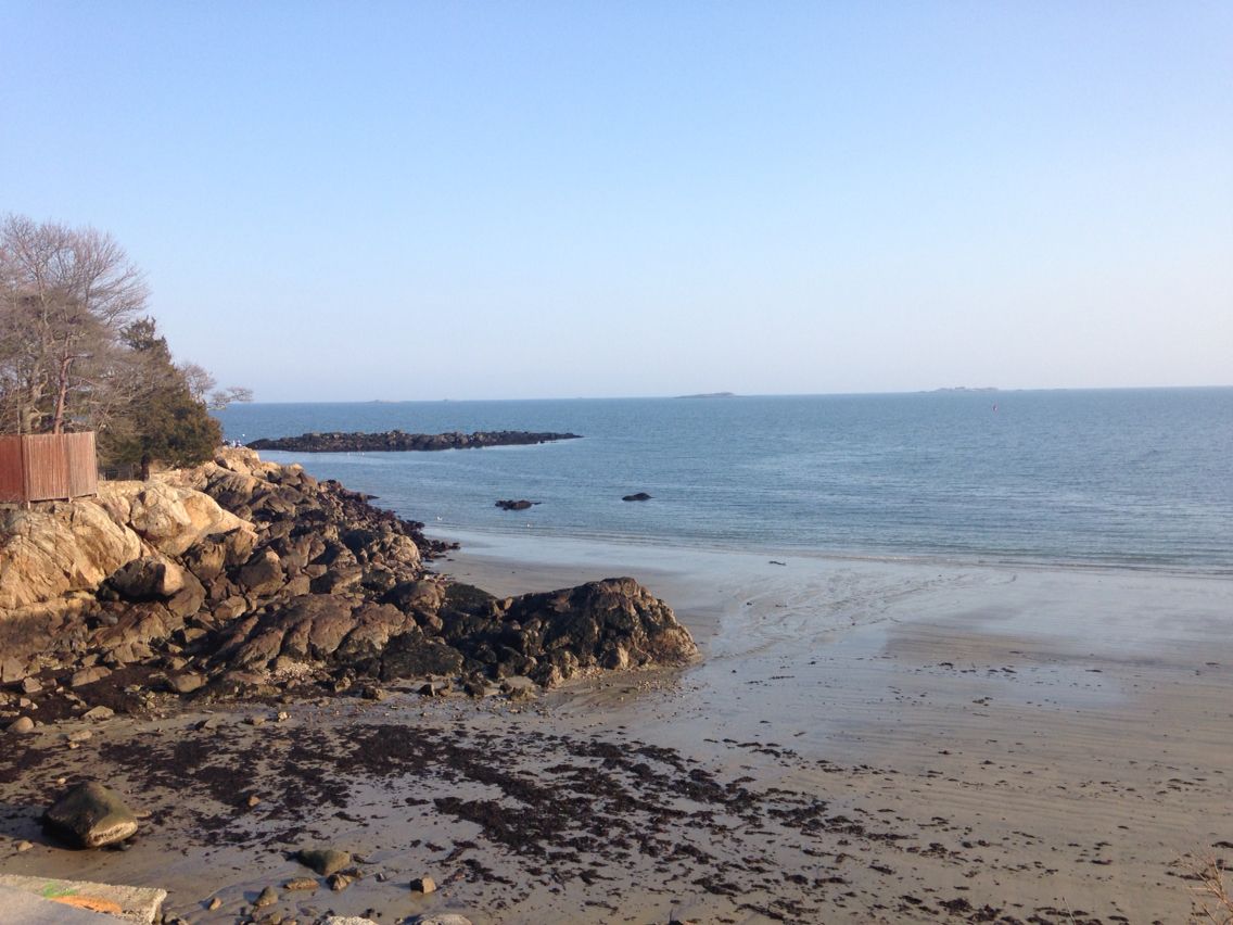 A quiet sand and rock beach on the Atlantic under a clear sky.