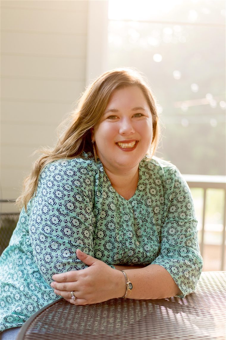 Erin Neuhardt, smiling, leaning on a table in warm backlight.