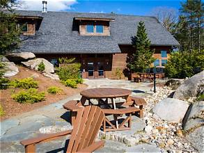 A stone patio with wooden Adirondack chairs and picnic tables set among boulders and pines.