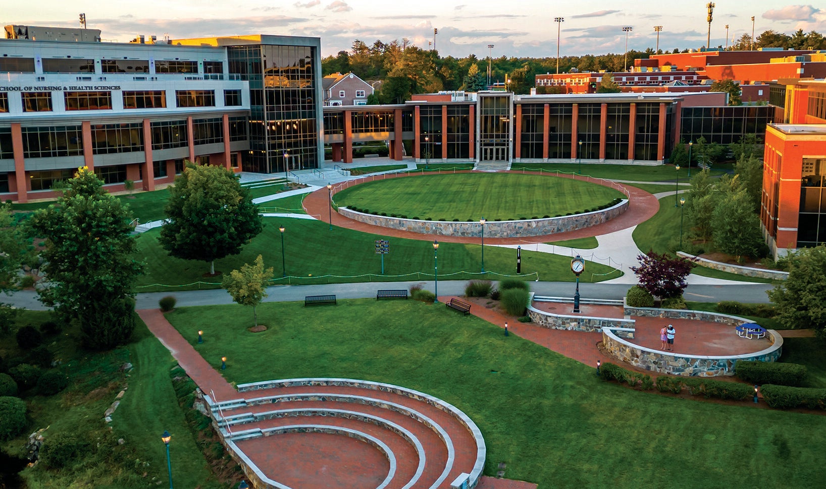 Endicott College quad at dusk — a circular lawn, curved stone amphitheater and lit buildings.
